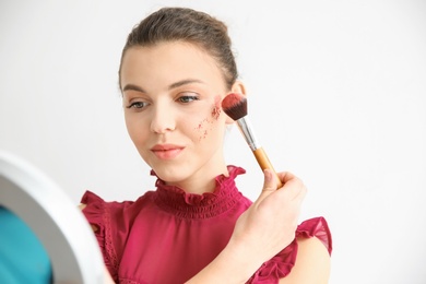 Photo of Young woman applying makeup on light background. Professional cosmetic products