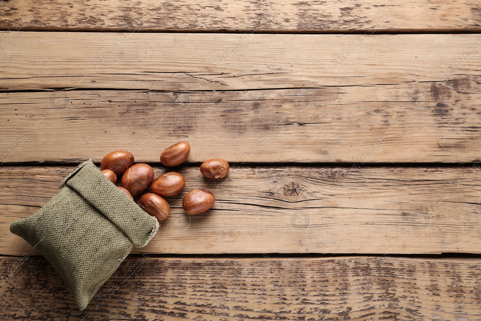 Photo of Overturned sackcloth bag with jackfruit seeds on wooden table, flat lay. Space for text