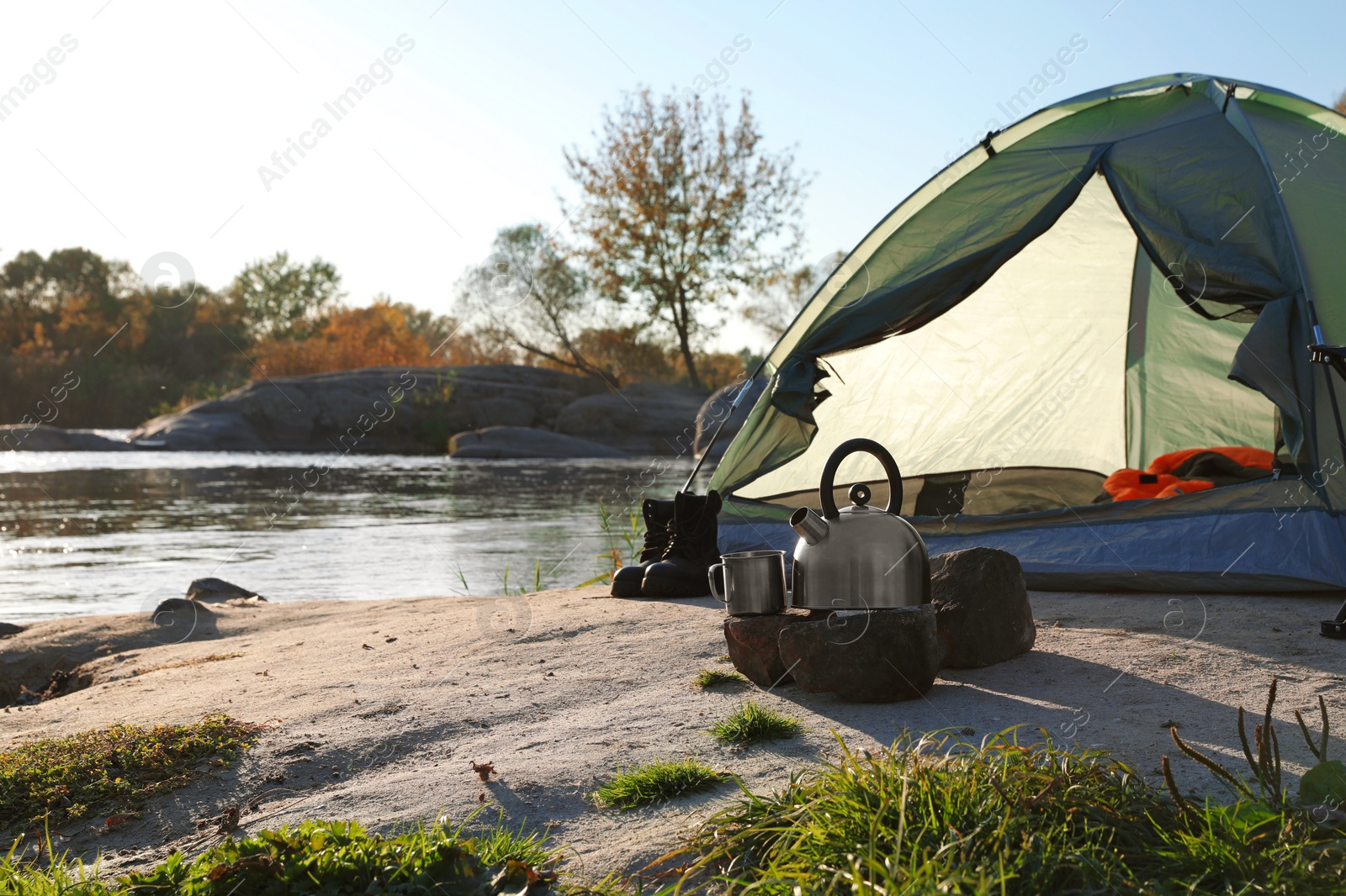 Photo of Kettle and mug on stones near tent with sleeping bag outdoors