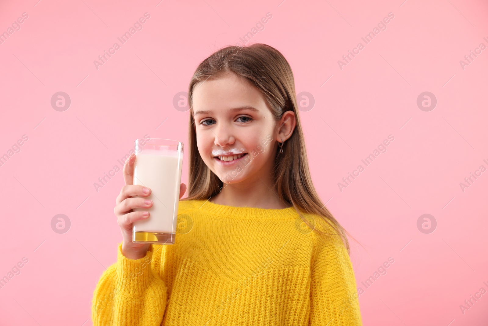 Photo of Happy little girl with milk mustache holding glass of tasty dairy drink on pink background