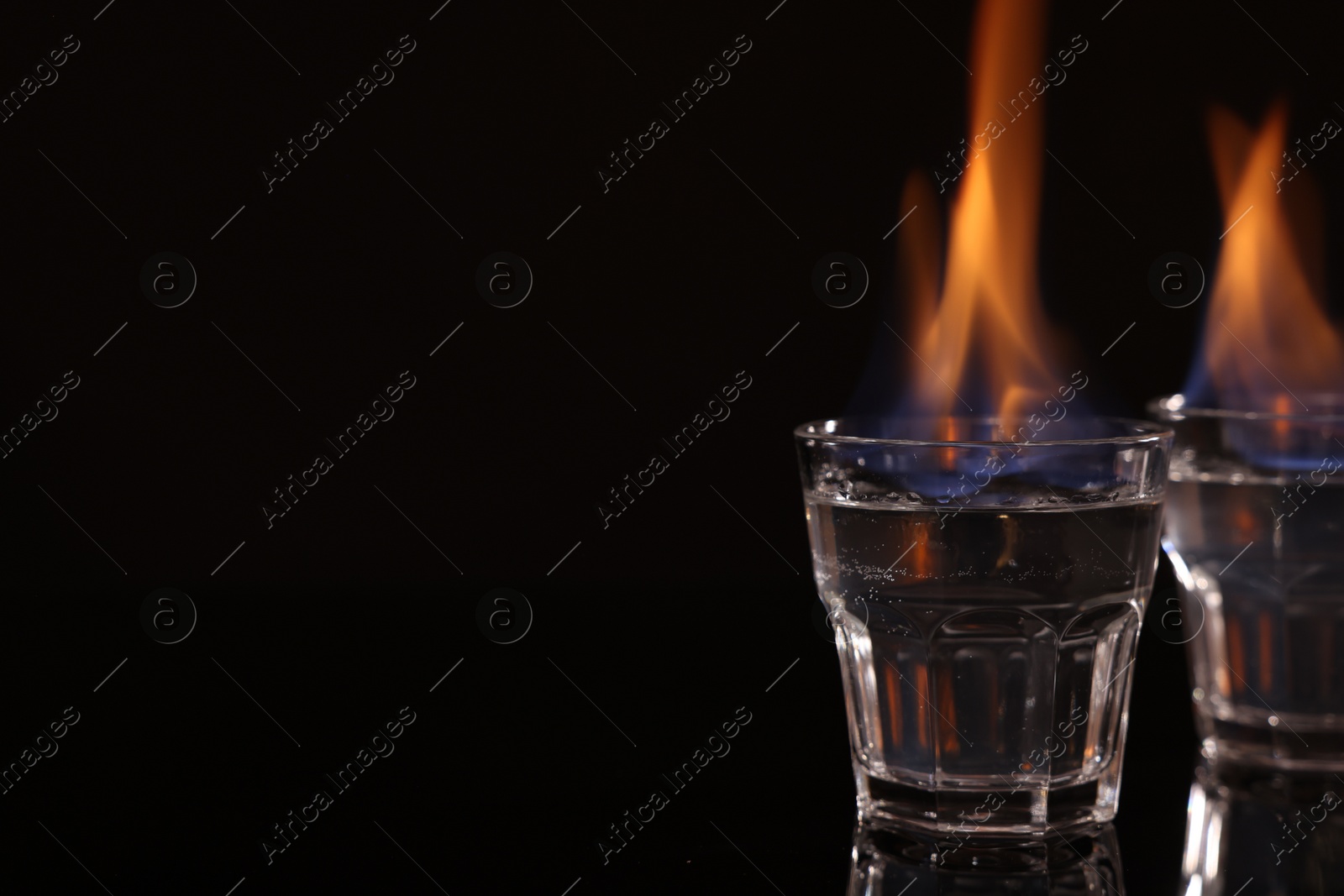 Photo of Flaming vodka in shot glasses on black background, space for text