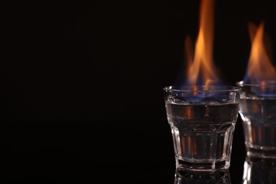 Flaming vodka in shot glasses on black background, space for text