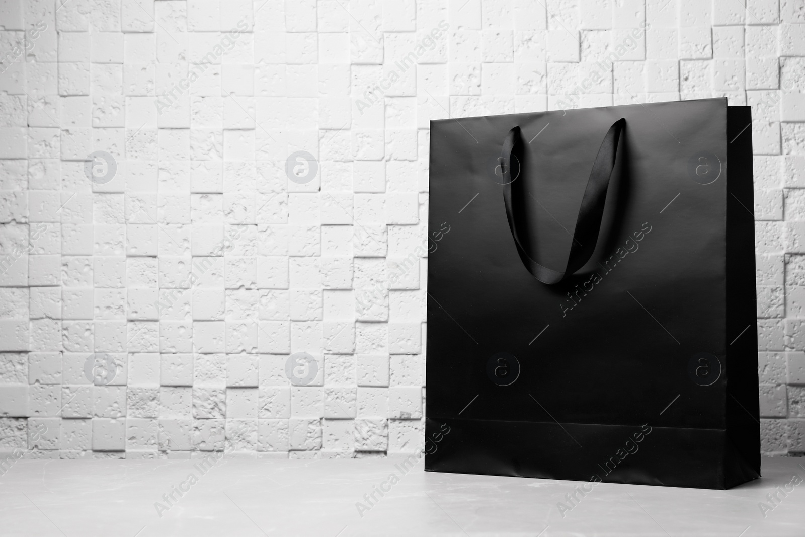 Photo of Paper shopping bag with ribbon handles on table near white wall. Mockup for design