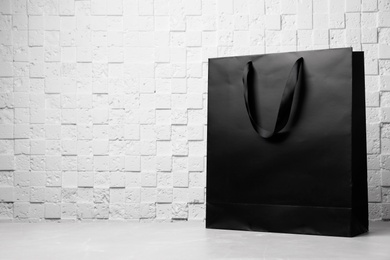 Photo of Paper shopping bag with ribbon handles on table near white wall. Mockup for design