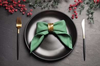 Photo of Plate with green fabric napkin, decorative ring and cutlery on black table, flat lay