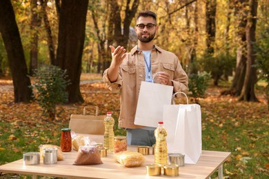 Photo of Portrait of volunteer with paper bag and food products on table in park