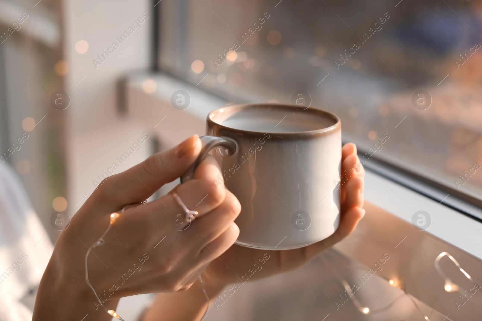 Photo of Young woman with cup of hot coffee near window, closeup