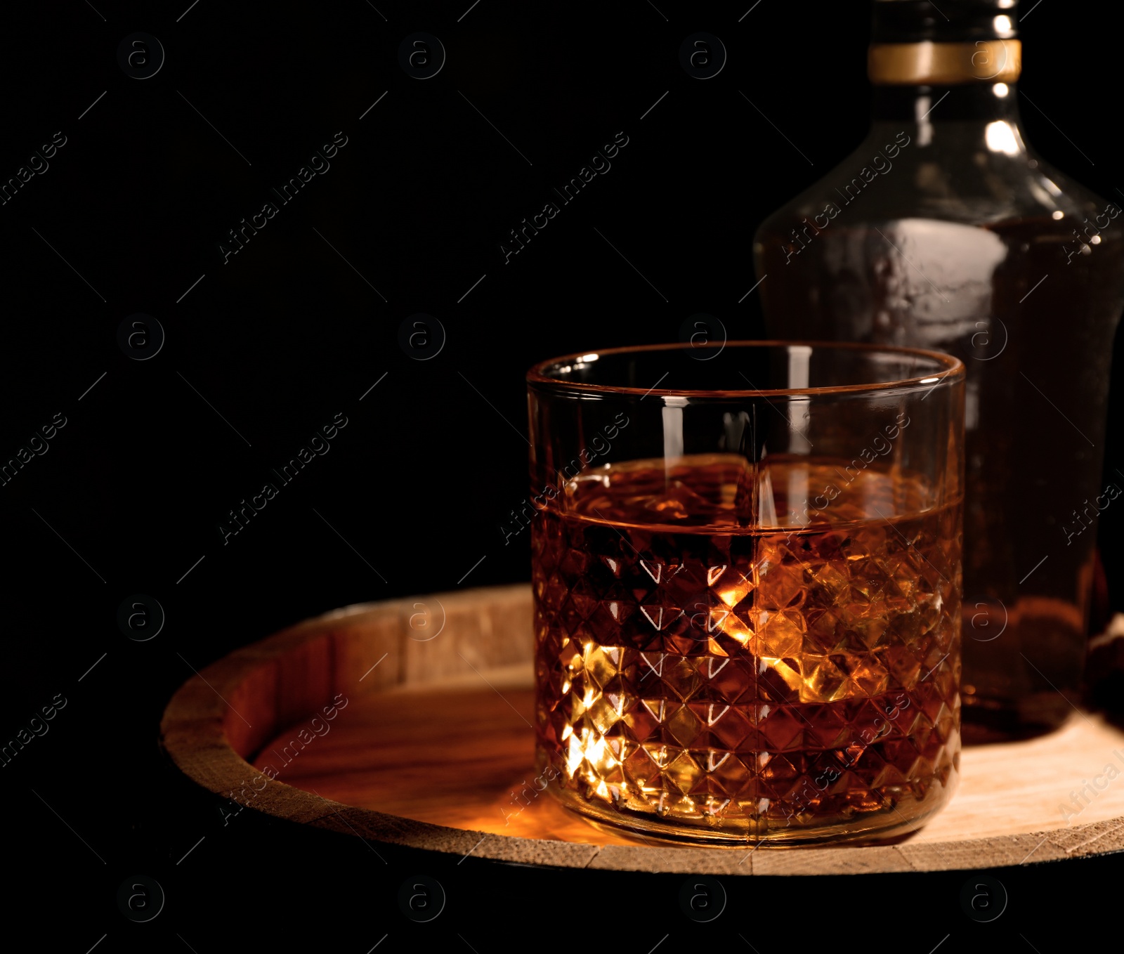 Photo of Golden whiskey in glass with ice cubes on wooden barrel. Space for text