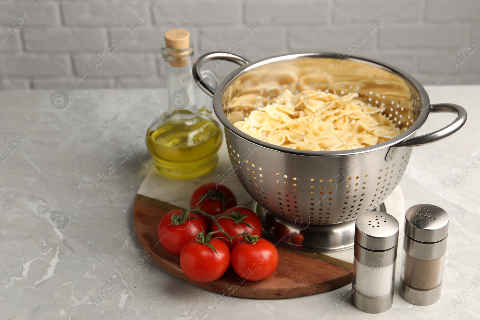 Photo of Cooked pasta in metal colander, spices, oil and tomatoes on grey table, closeup. Space for text