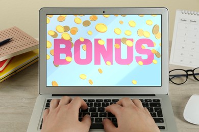 Image of Bonus gaining. Woman using laptop at wooden table, closeup. Illustration of falling coins and word on device screen