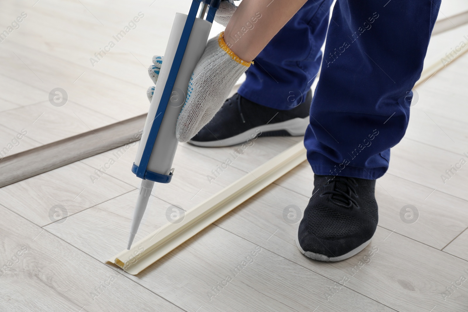 Photo of Man using caulking gun while installing plinth on laminated floor in room, closeup