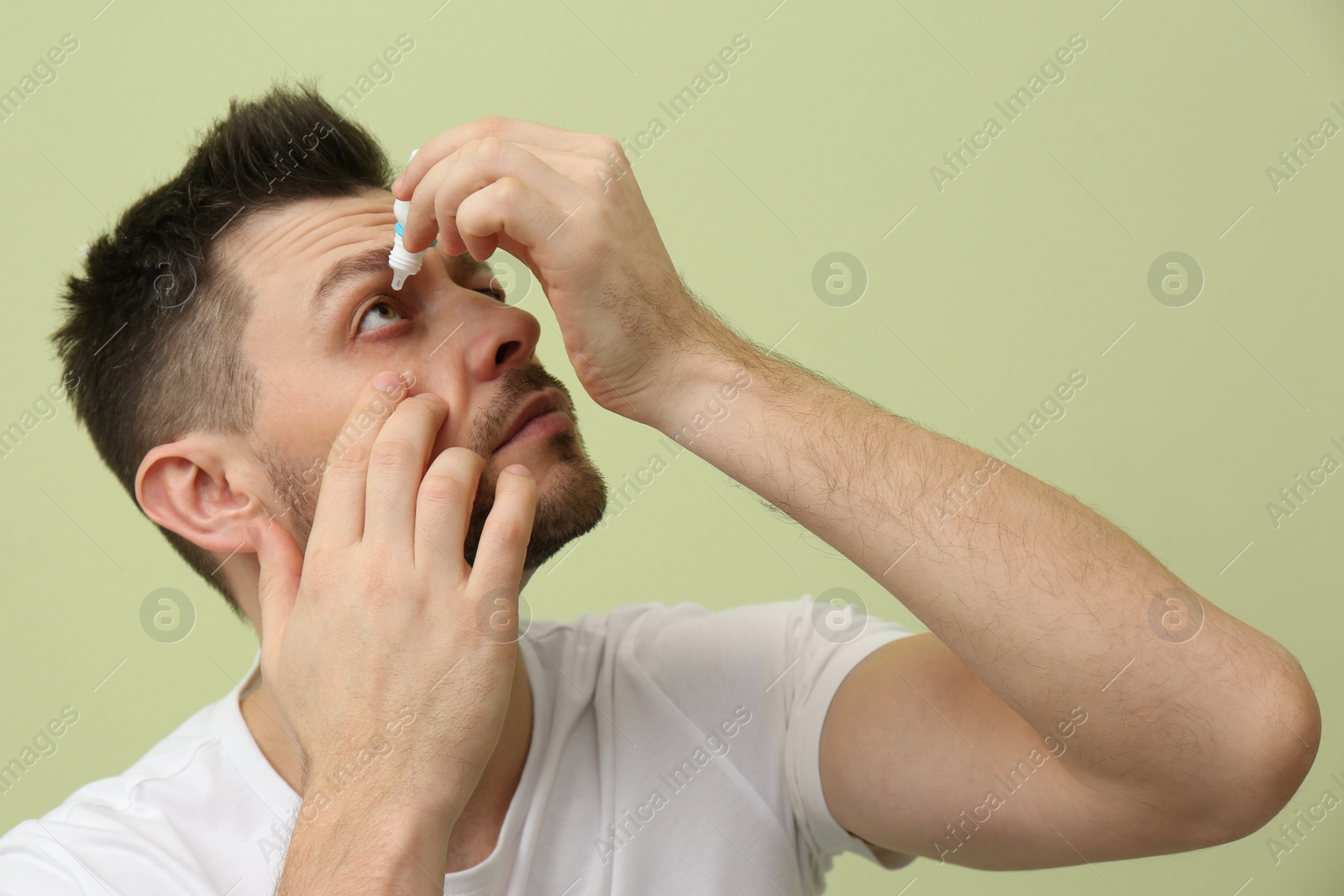 Photo of Man using eye drops on light green background