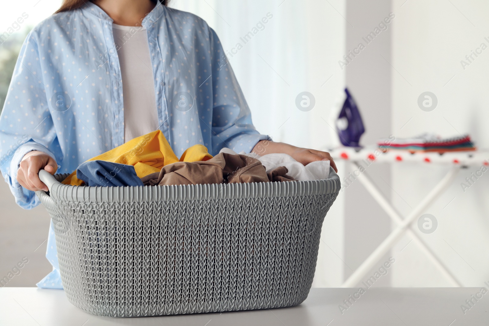 Photo of Woman with basket full of clean laundry at table indoors, closeup