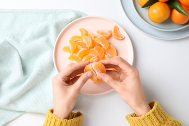 Photo of Woman holding fresh juicy tangerine at white table, top view