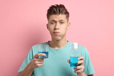 Young man using mouthwash on pink background