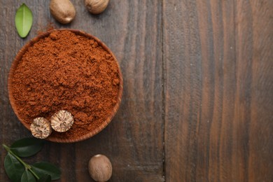 Photo of Nutmeg powder in bowl, seeds and green leaves on wooden table, flat lay. Space for text