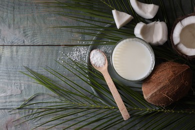 Glass of delicious coconut milk, spoon with flakes, nuts and palm leaves on wooden table, flat lay. Space for text