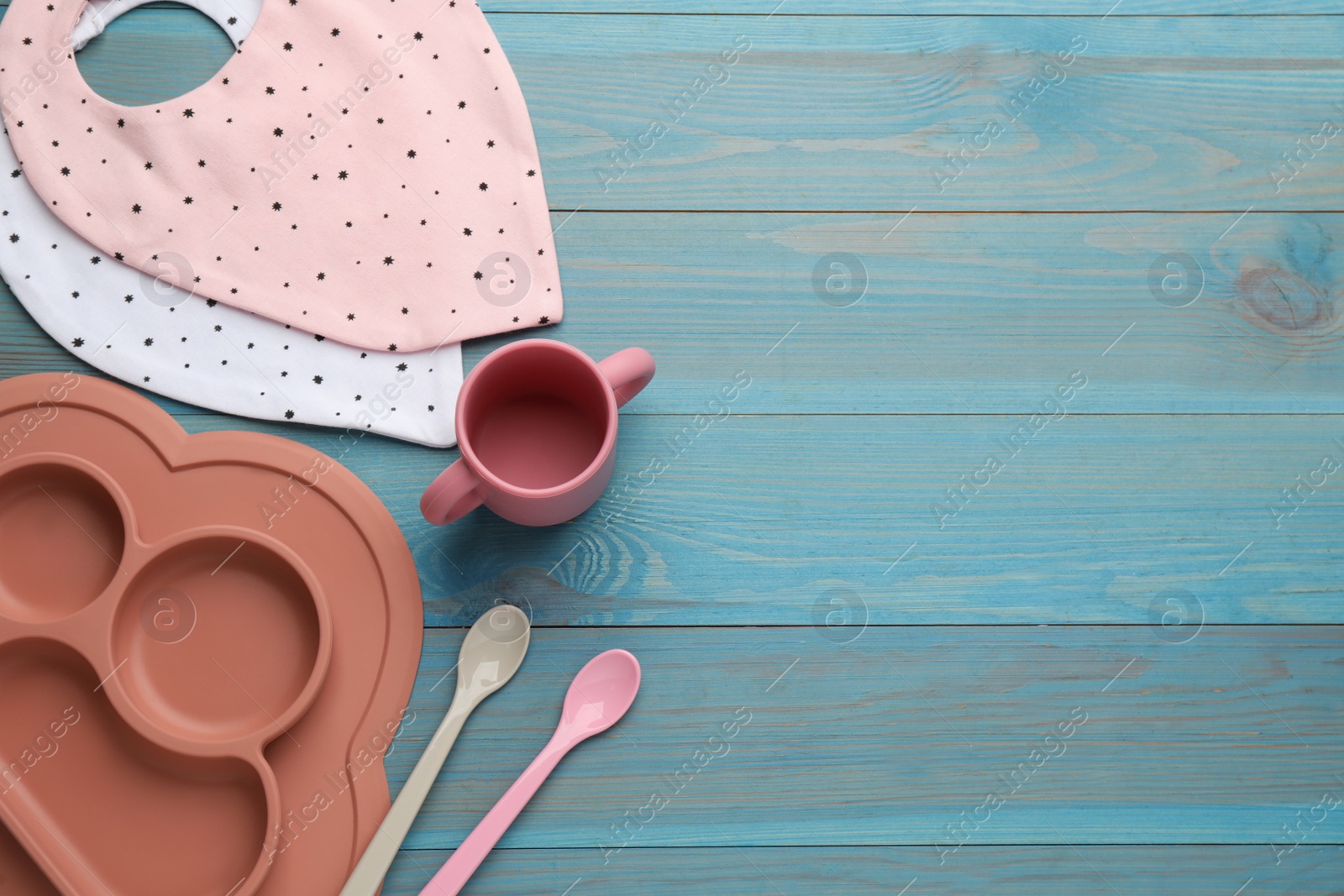 Photo of Flat lay composition with drool baby bibs and plastic dishware on light blue wooden background. Space for text