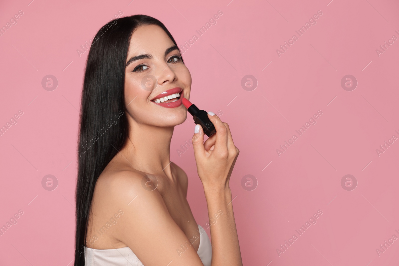 Photo of Young woman with beautiful makeup holding glossy lipstick on pink background. Space for text