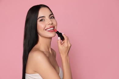 Photo of Young woman with beautiful makeup holding glossy lipstick on pink background. Space for text
