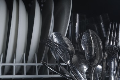 Photo of Clean wet plates and cutlery in dishwasher, closeup