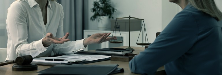 Lawyer working with client at wooden table in office, closeup. Banner design