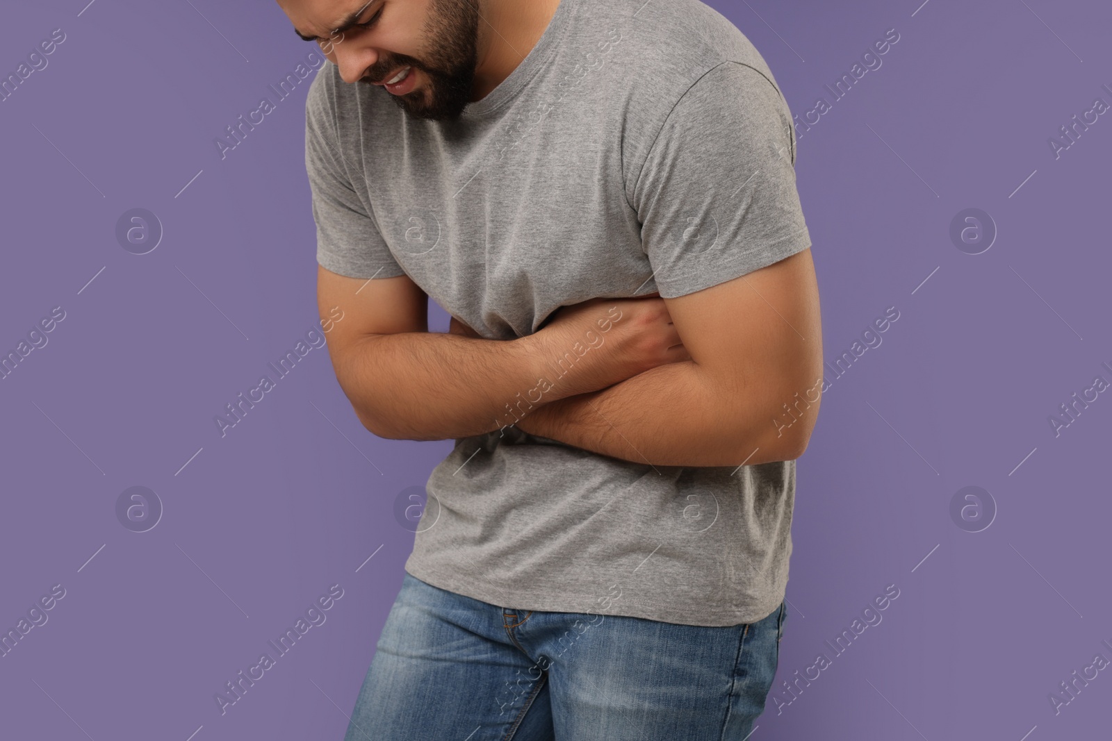 Photo of Young man suffering from stomach pain on purple background