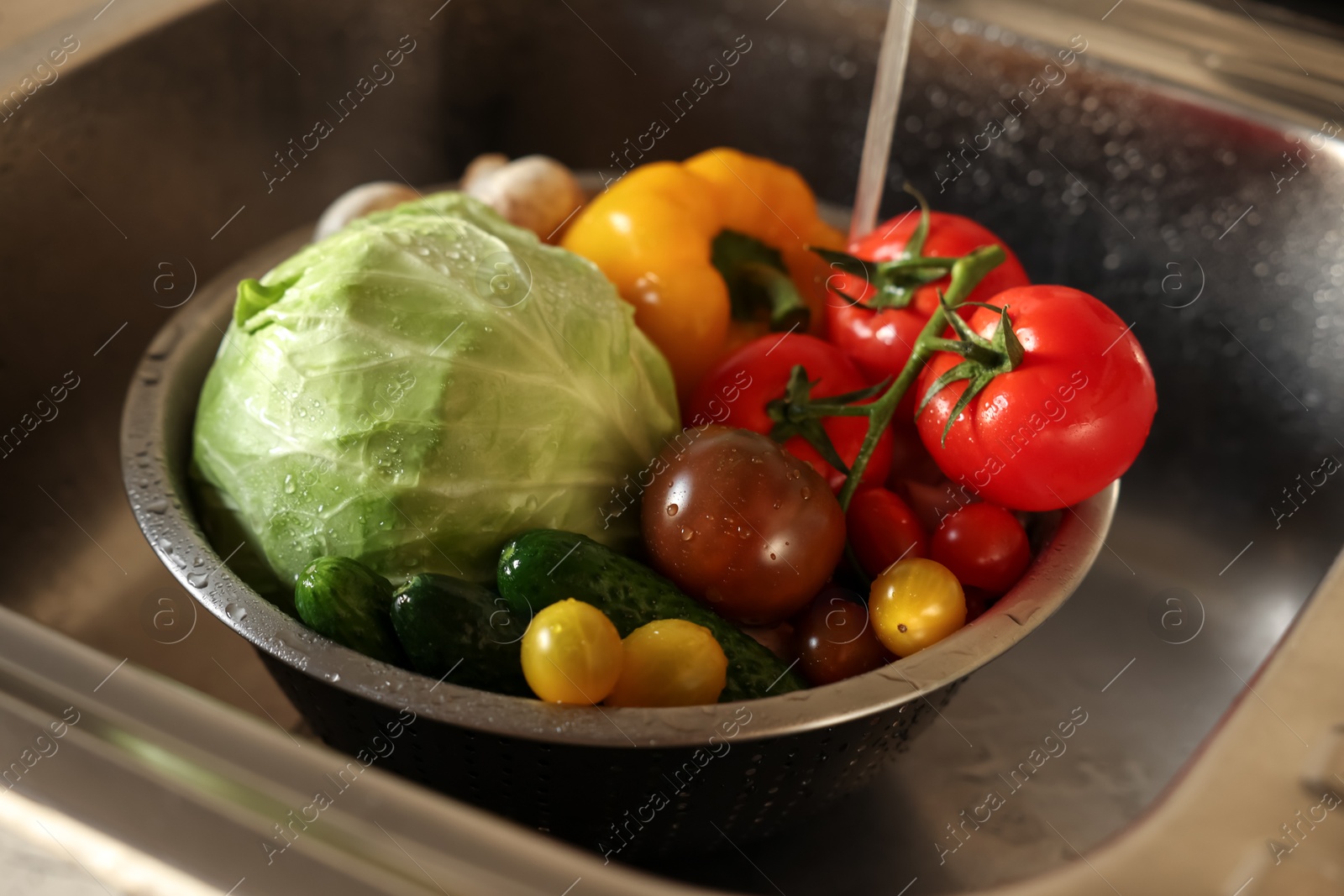 Photo of Washing different vegetables with tap water in metal colander inside sink