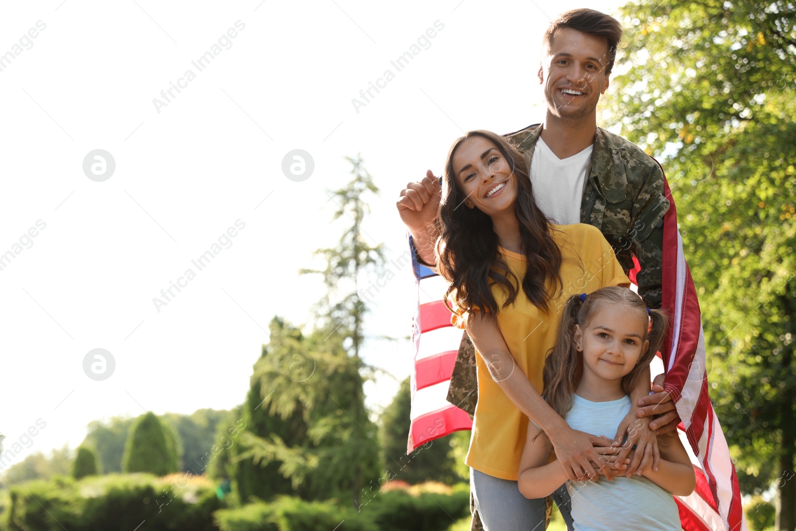 Photo of Man in military uniform with American flag and his family at sunny park