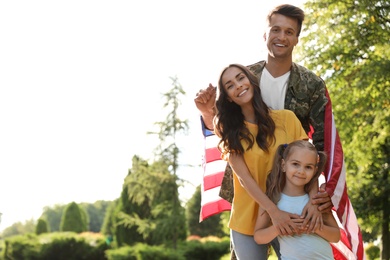 Photo of Man in military uniform with American flag and his family at sunny park