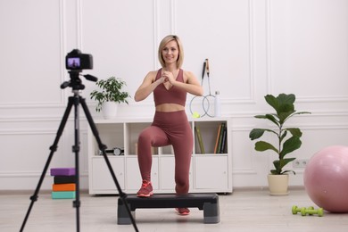 Smiling sports blogger recording fitness lesson with camera at home