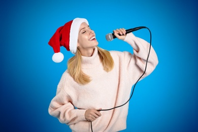 Photo of Happy woman in Santa Claus hat singing with microphone on blue background. Christmas music