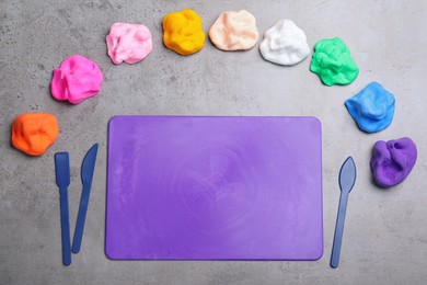 Many different colorful plasticine pieces with tools on grey table, flat lay