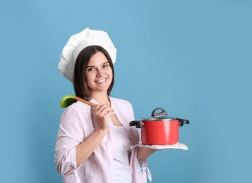 Photo of Happy young woman with cooking pot and ladle on light blue background. Space for text