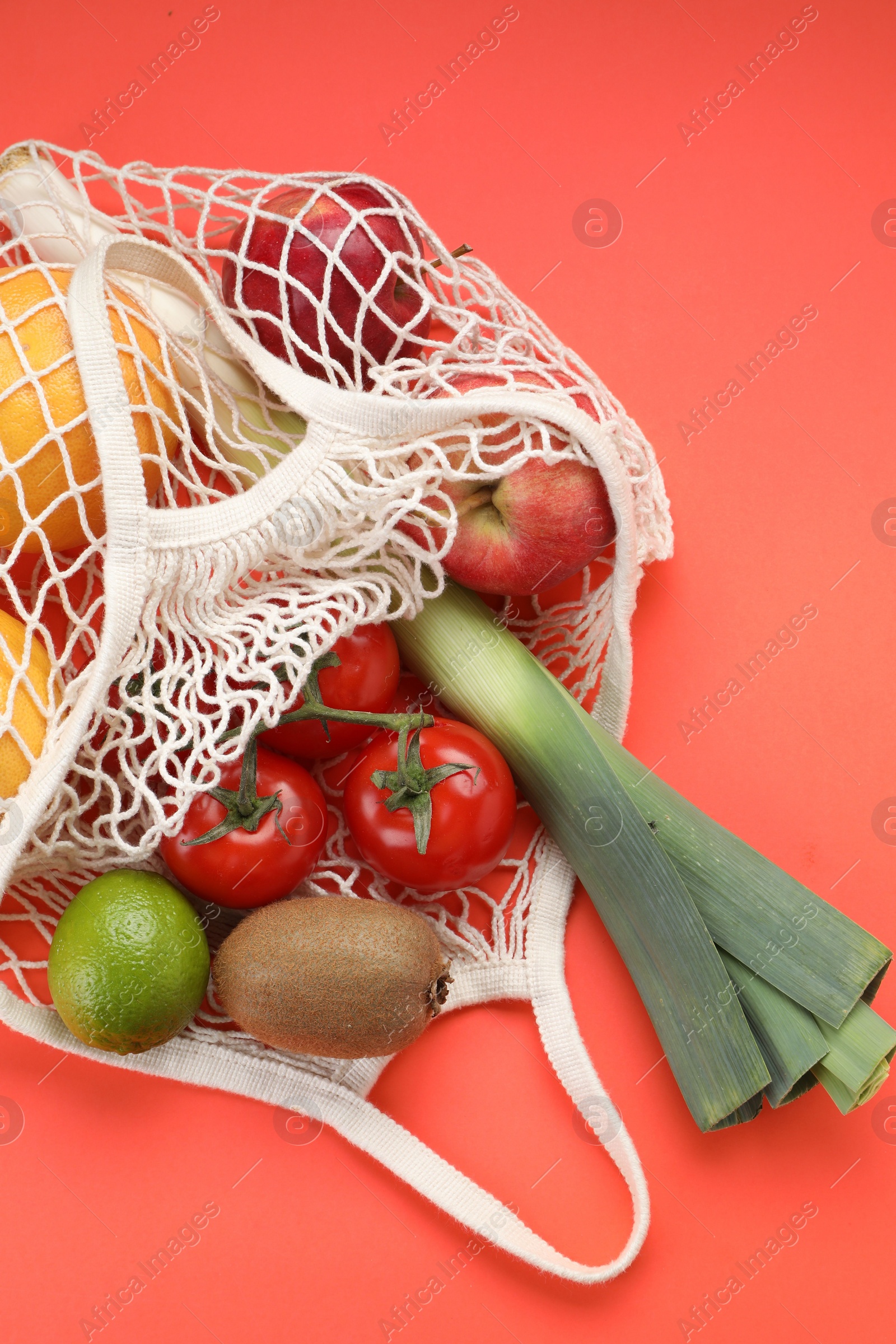 Photo of String bag with different vegetables and fruits on red background, top view