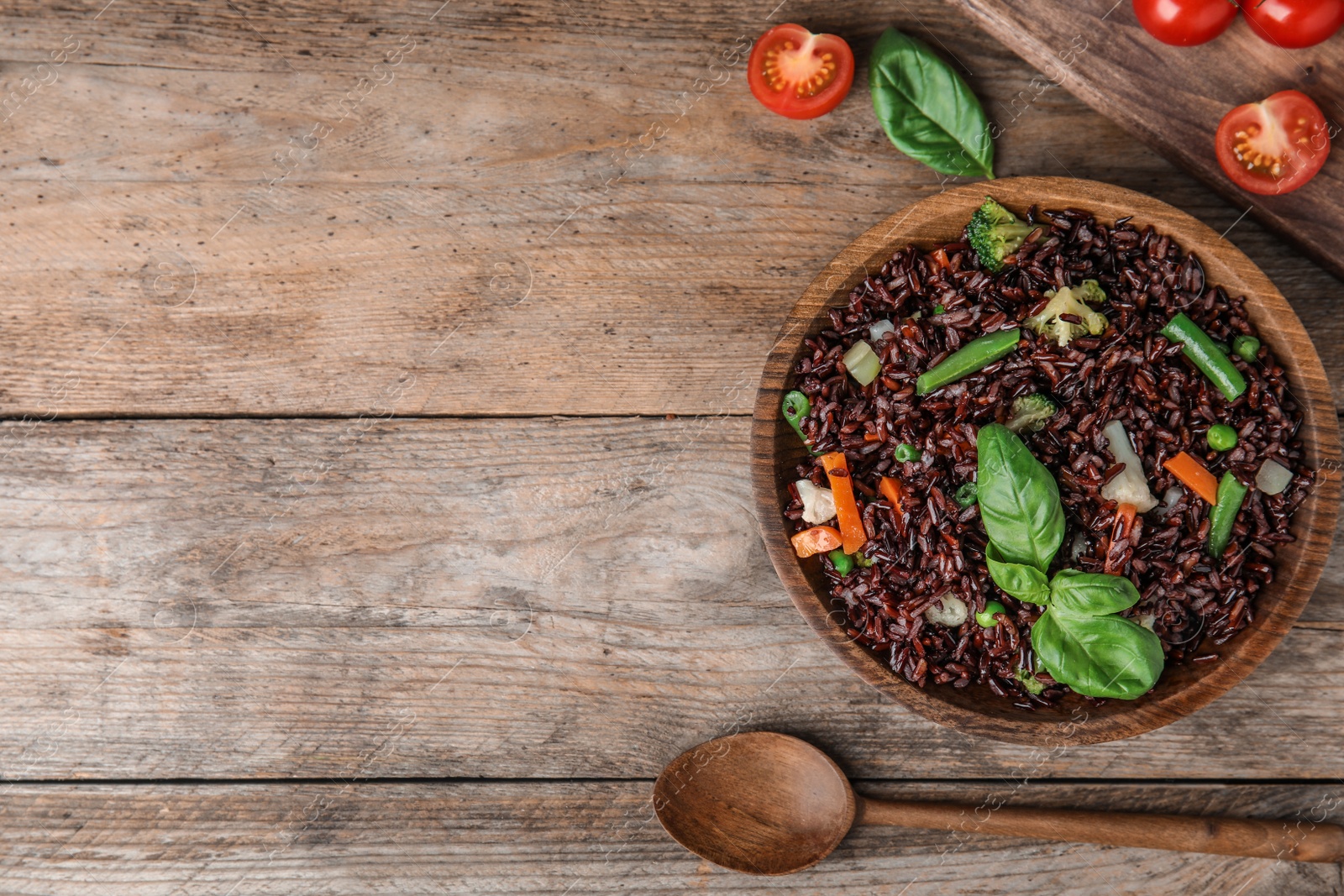 Photo of Plate of brown rice with vegetables served on wooden table, flat lay. Space for text