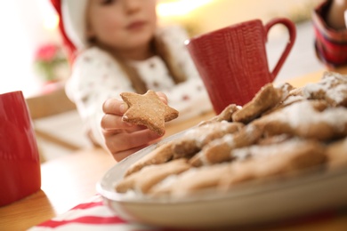 Little girl taking tasty Christmas cookie from plate at table, closeup