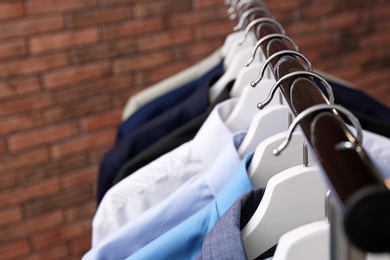 Wardrobe rack with stylish clothes near brick wall, closeup. Space for text