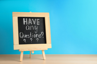 Photo of Blackboard with phrase HAVE ANY QUESTIONS on wooden table against blue background. Space for text
