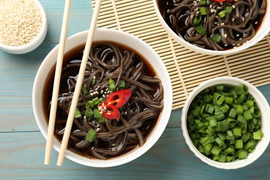 Photo of Tasty buckwheat noodle (soba) soup with chili pepper, green onion, sesame and chopsticks on light blue wooden table, flat lay