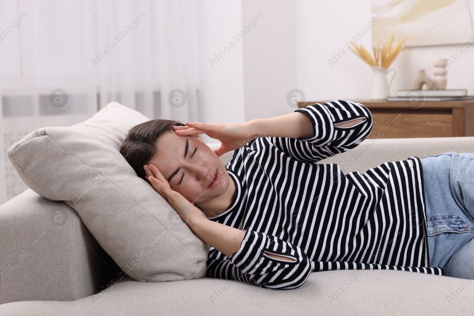 Photo of Sad woman suffering from headache on sofa indoors