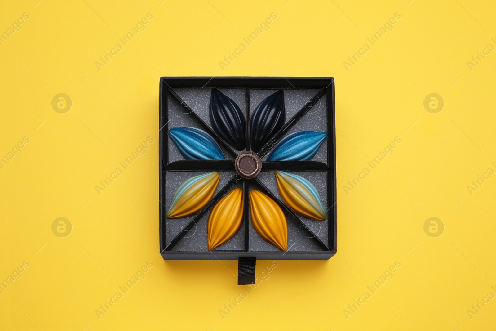 Photo of Box of tasty chocolate candies on yellow background, top view