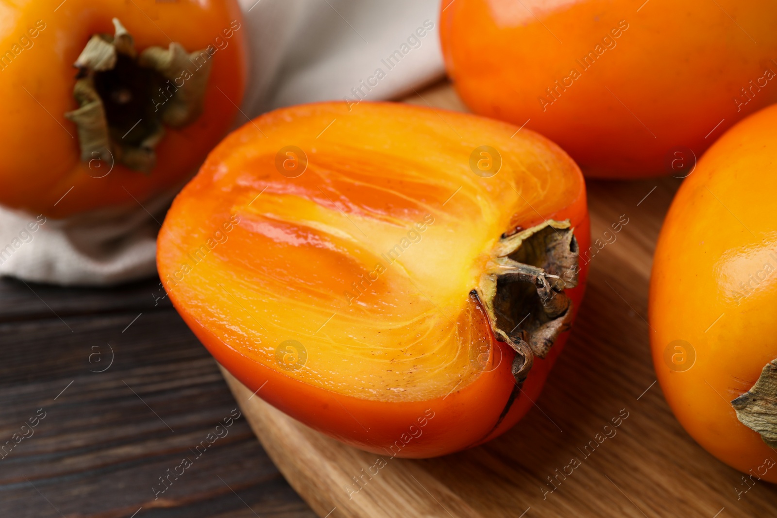 Photo of Whole and cut delicious ripe persimmons on wooden table, closeup