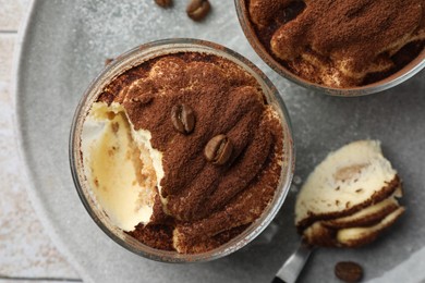 Delicious tiramisu in glasses, spoon and coffee beans on table, top view