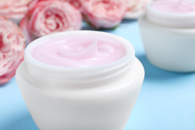 Photo of Open jars of cream and flowers on blue background, closeup