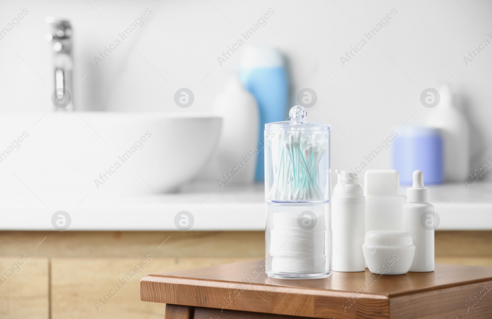 Photo of Cotton pads and swabs near cosmetic products on wooden stool in bathroom. Space for text