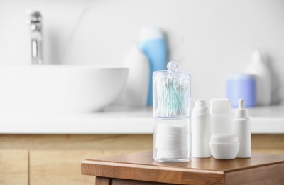 Cotton pads and swabs near cosmetic products on wooden stool in bathroom. Space for text