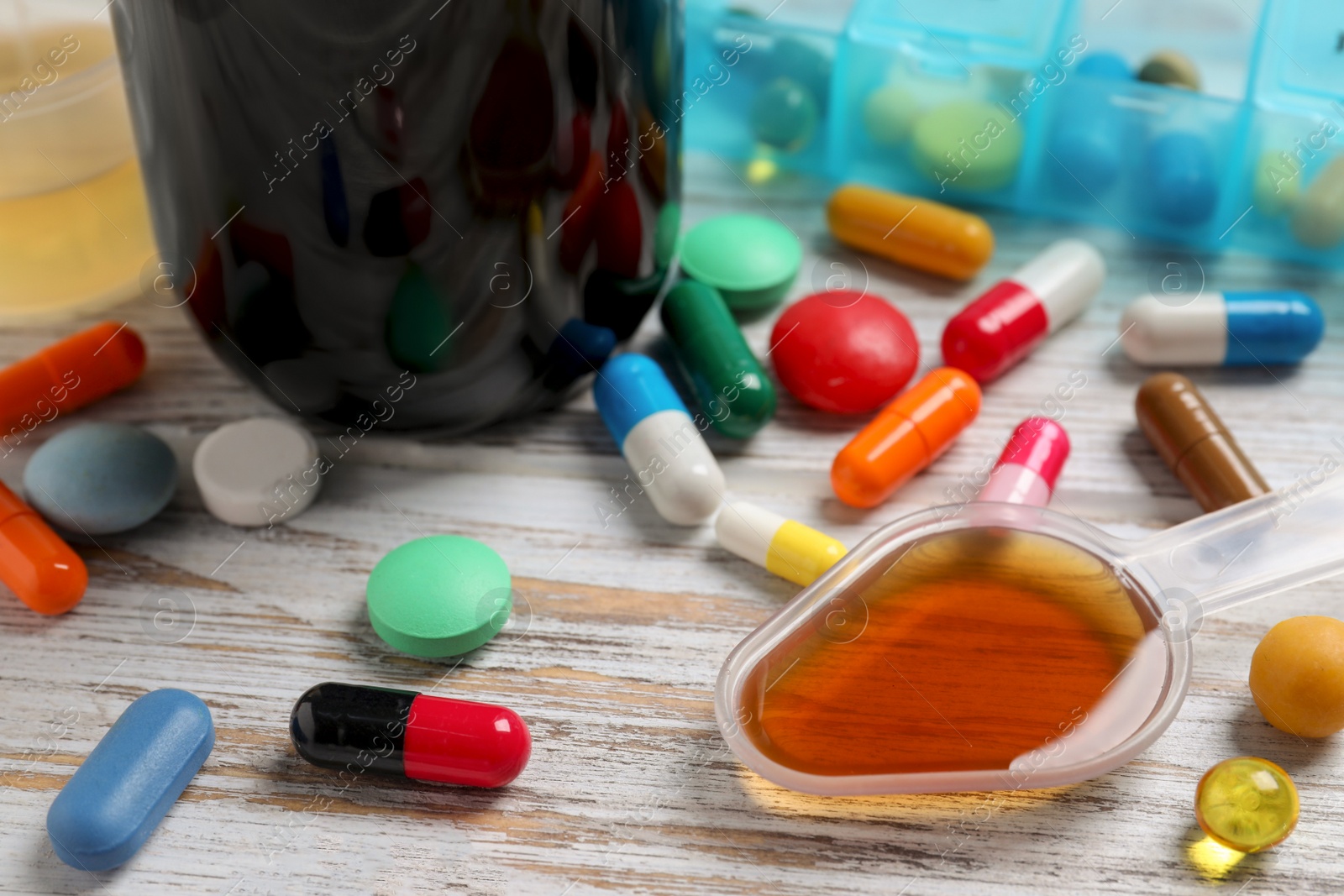 Photo of Dosing spoon with syrup and pills on white wooden table, closeup. Cold medicine