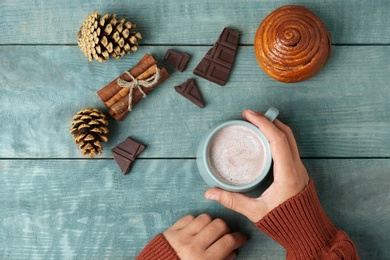 Photo of Woman with cup of delicious cocoa drink at light blue wooden table, top view