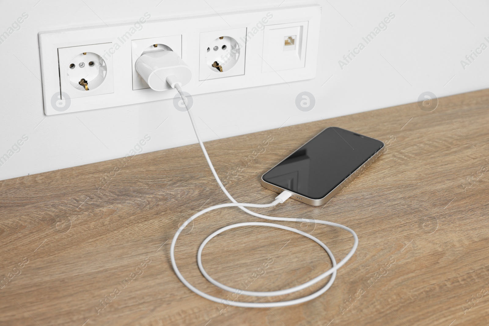 Photo of Modern mobile phone charging on wooden table